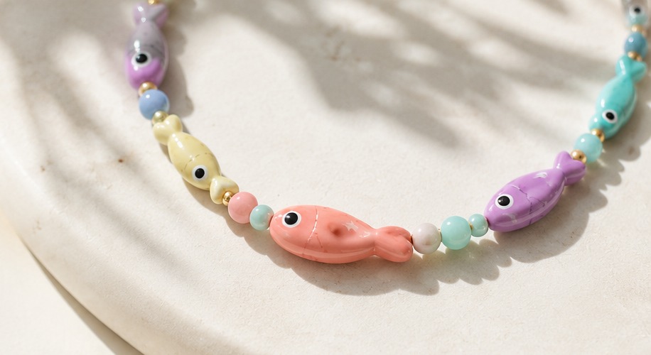 Close up of a coral fish bead between gold spacers and pale stone rounds in raking sunlight.