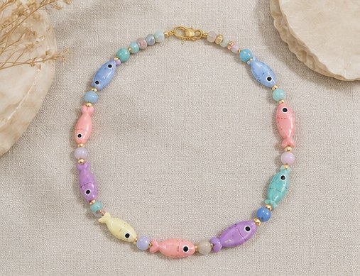 Pastel porcelain fish necklace laid flat, with a gold clasp and stone spacer beads.